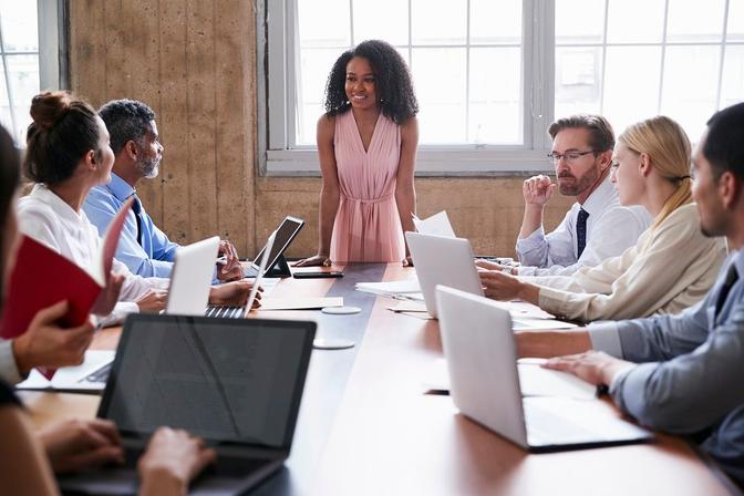 A woman confidently leading a group of people at a conference table, engaging in a productive discussion.