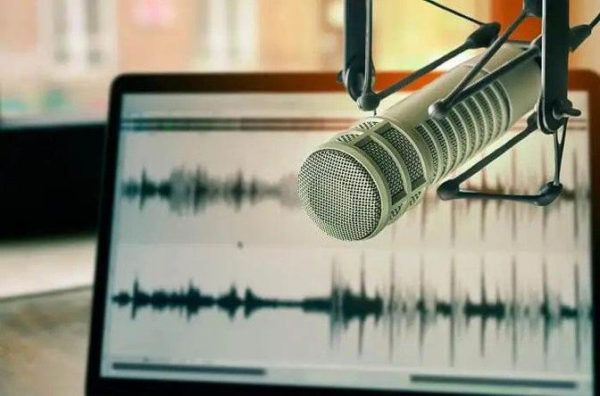 Microphone for audio recording sits on a desk in front of a laptop computer displaying sound waves on its screen.