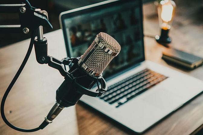 A close-up photo of a black microphone and a silver laptop computer on a brown wooden table.