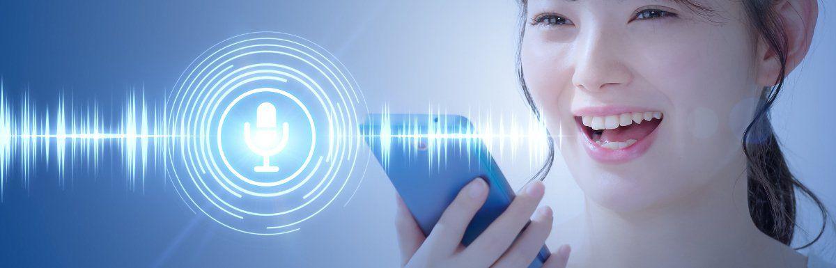 A young woman smiling while using her smartphone, with a digital illustration of a microphone and sound waves overlaying a blue background, representing voice recognition technology.