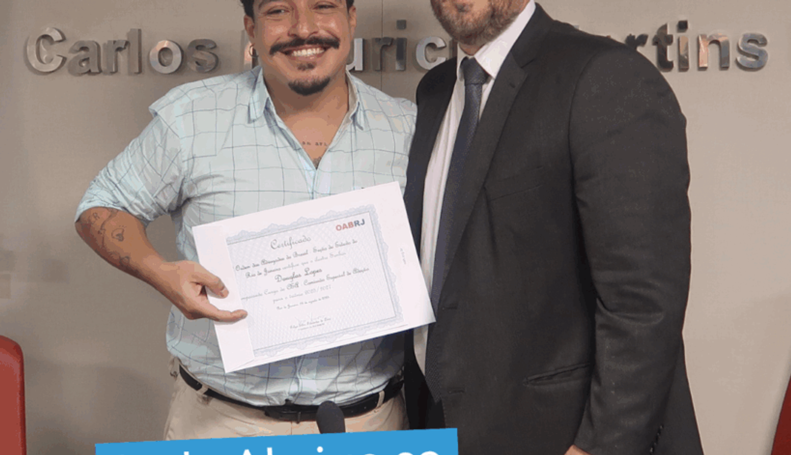 Dois homens posam lado a lado em frente ao painel da OAB-RJ. Um deles segura um certificado enquanto o outro, de terno e gravata, está ao seu lado. Na parte inferior da imagem, aparece a frase: “Rede Abrigo se torna consultora da comissão de adoção da OAB Rio”.