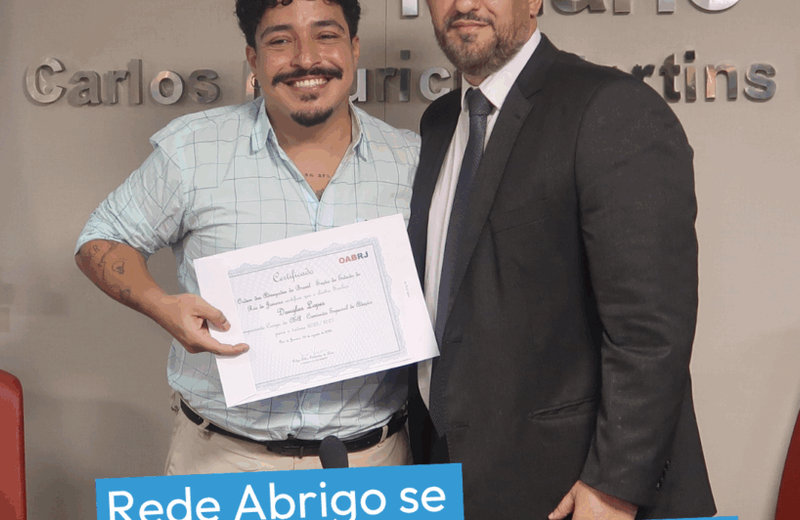 Dois homens posam lado a lado em frente ao painel da OAB-RJ. Um deles segura um certificado enquanto o outro, de terno e gravata, está ao seu lado. Na parte inferior da imagem, aparece a frase: “Rede Abrigo se torna consultora da comissão de adoção da OAB Rio”.