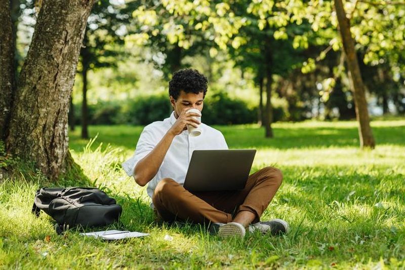 A guy sitting in the park drinking a cup of coffee.