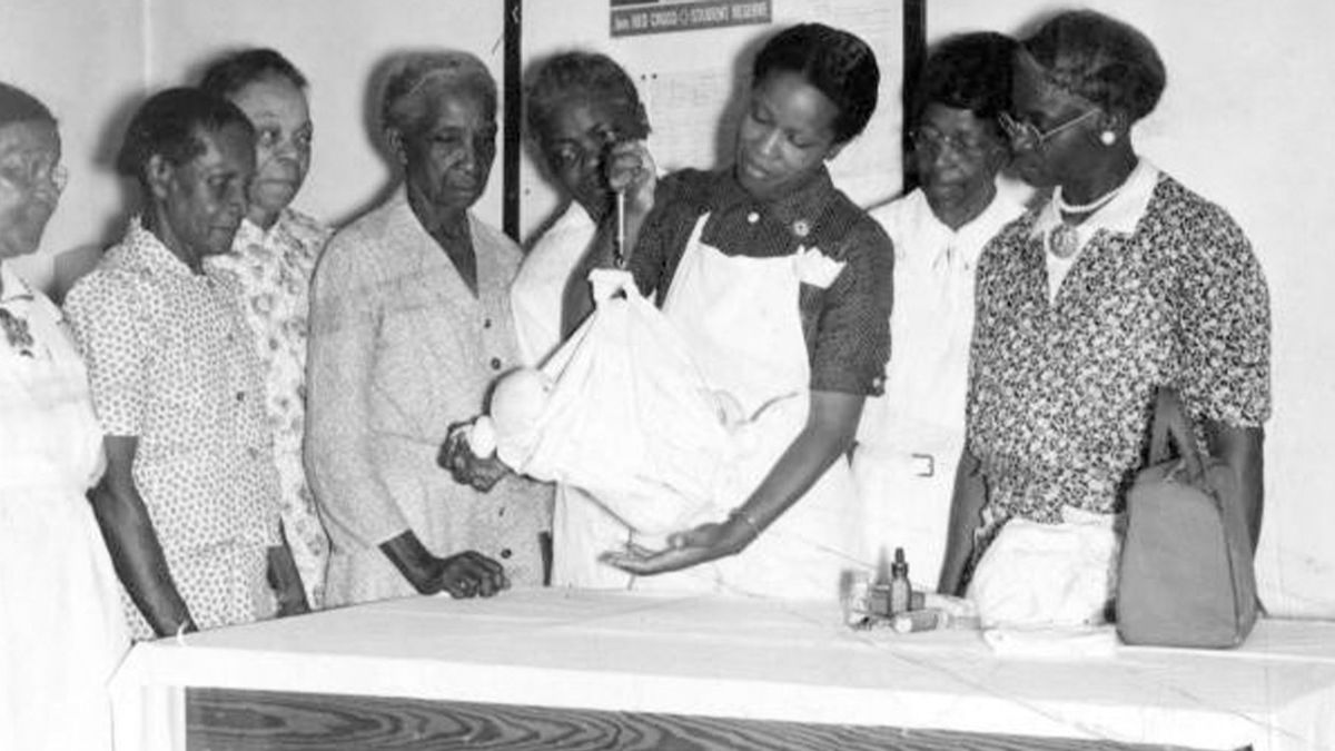 A black nurse showing black midwives how to use a portable scale to weigh babies.