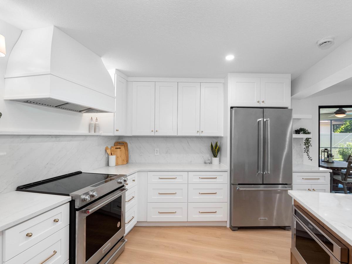 Modern kitchen with white cabinetry, marble backsplash, stainless steel appliances, and wood flooring