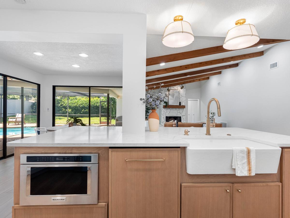 Kitchen island with farmhouse sink, wood cabinetry, and exposed ceiling beams opening to living room
