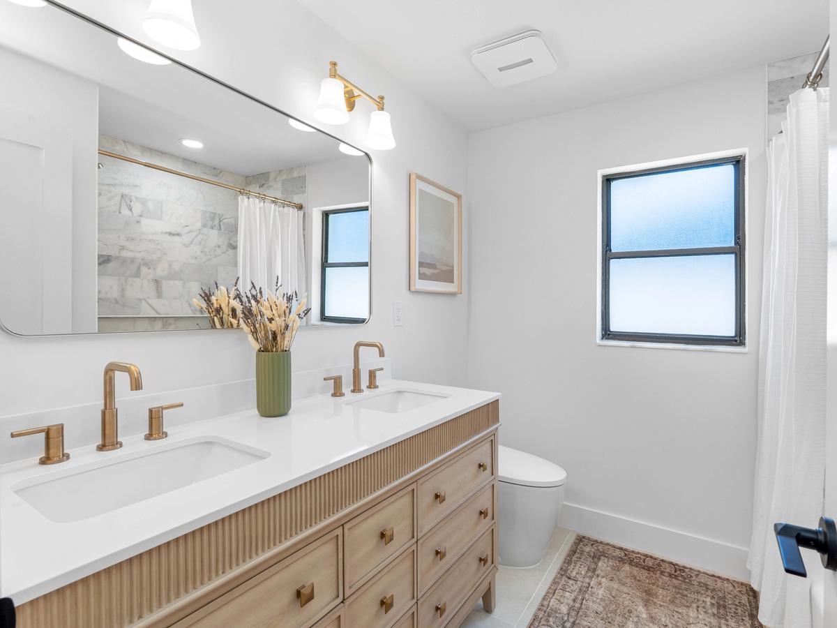 Bathroom with double vanity, wood cabinetry, brass fixtures, and marble countertop in renovated Clearwater home