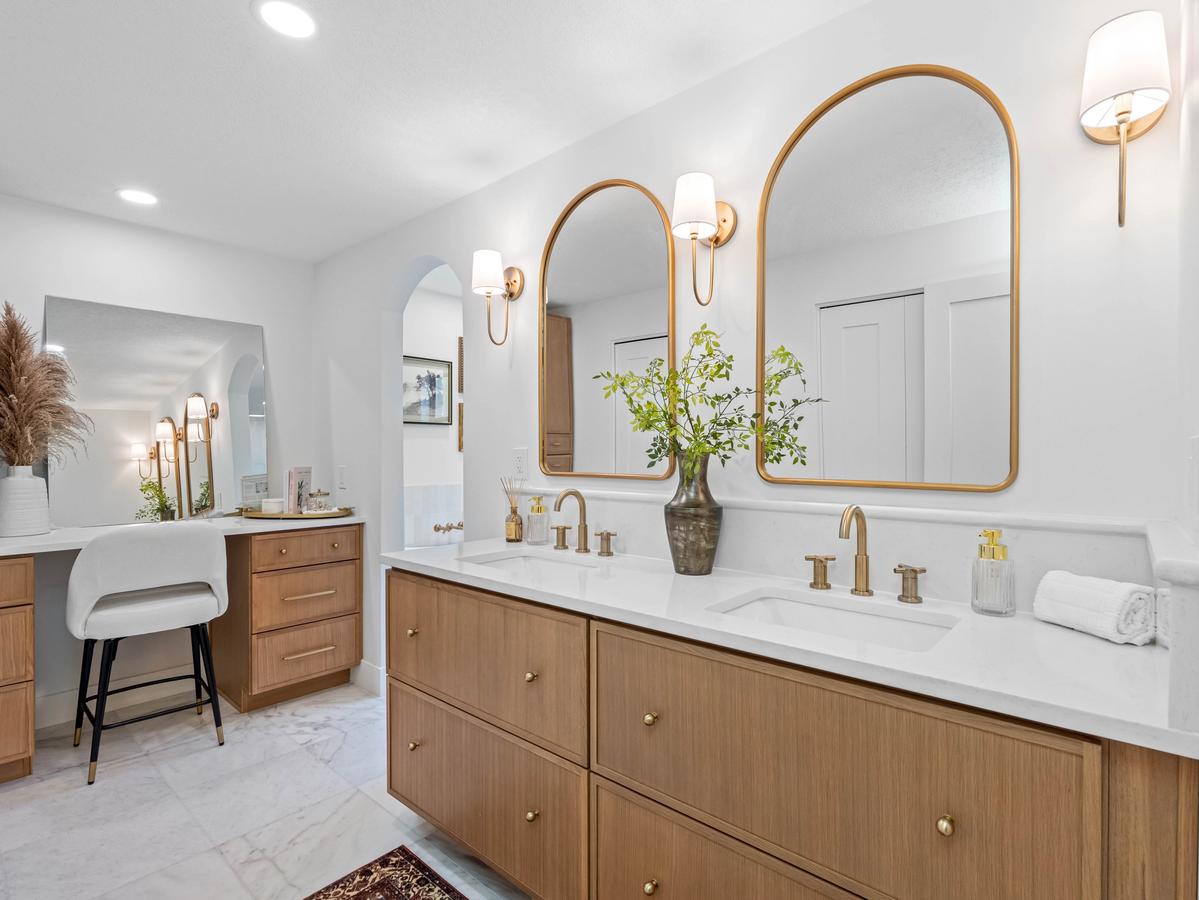 Modern bathroom renovation with double vanity, warm wood cabinetry, brass fixtures, and arched mirrors in Clearwater home
