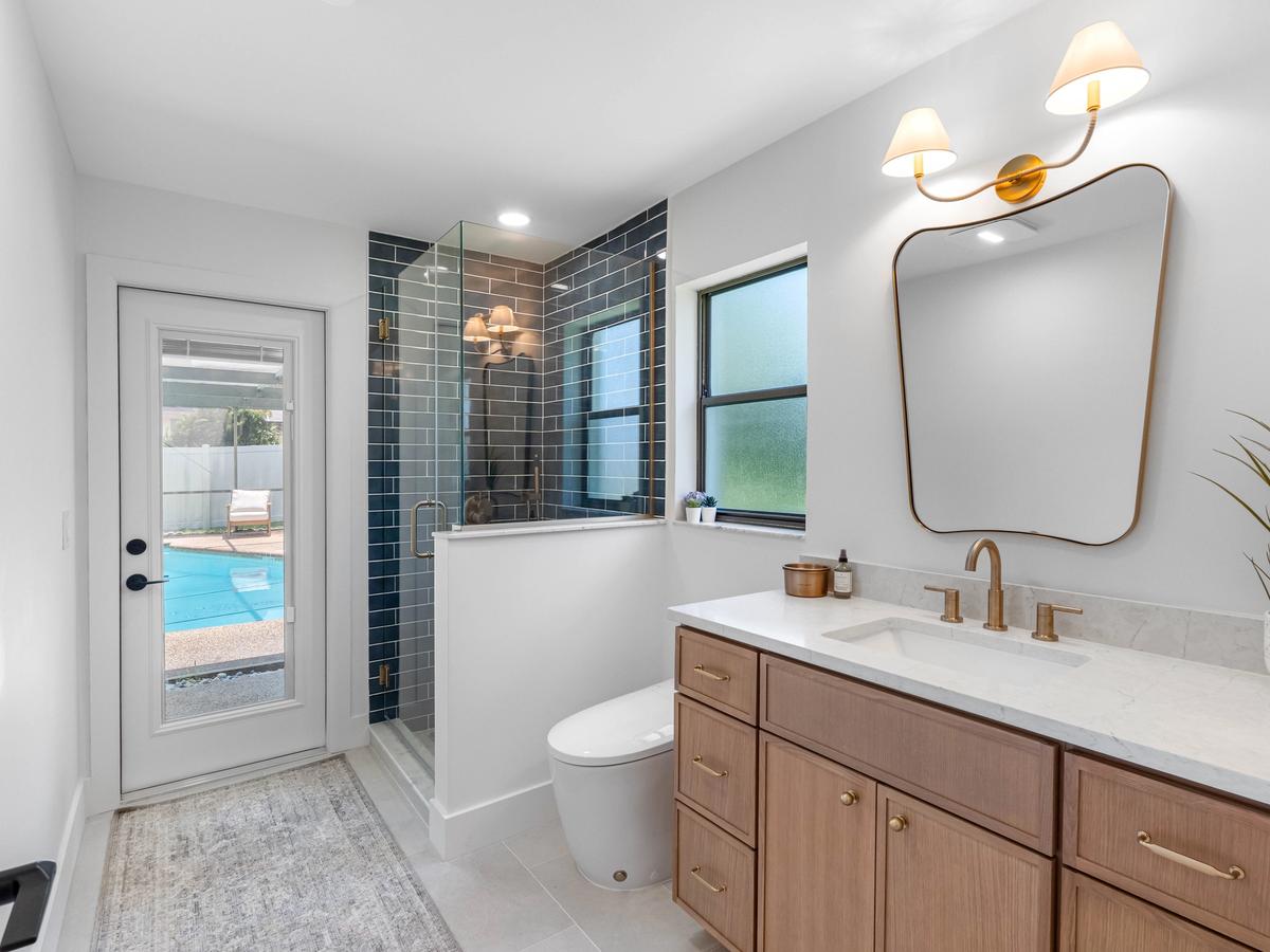 Bathroom with glass shower, dark tile walls, wood vanity, and view to outdoor pool area
