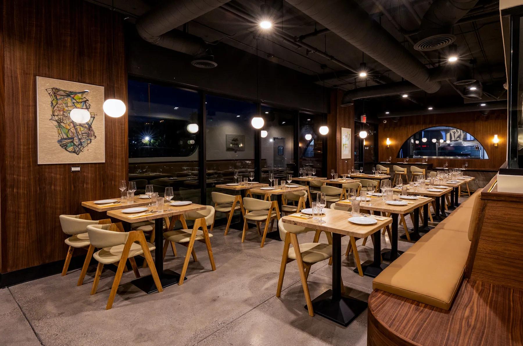 The Pizzeria Sei dining room set for an evening service, warm pendant lighting over wood-topped tables