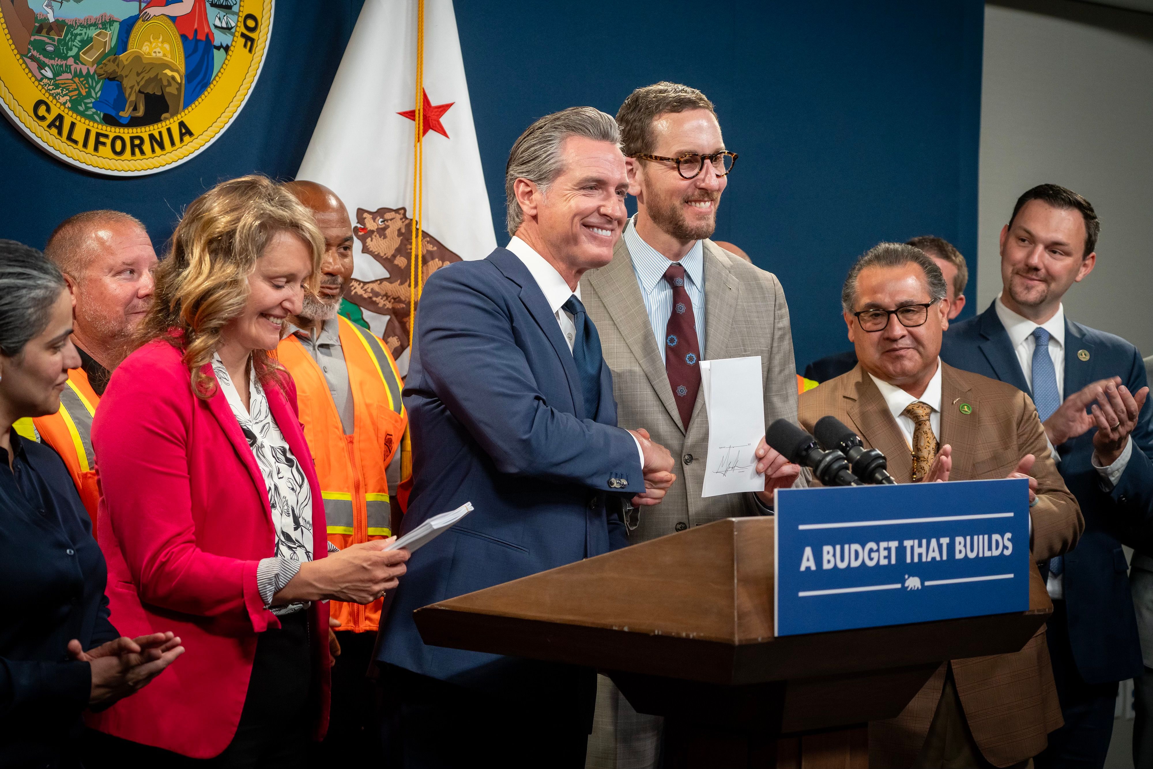 Governor Newsom shakes hands with California Senator Scott Wiener after signing AB 130 and SB 131.