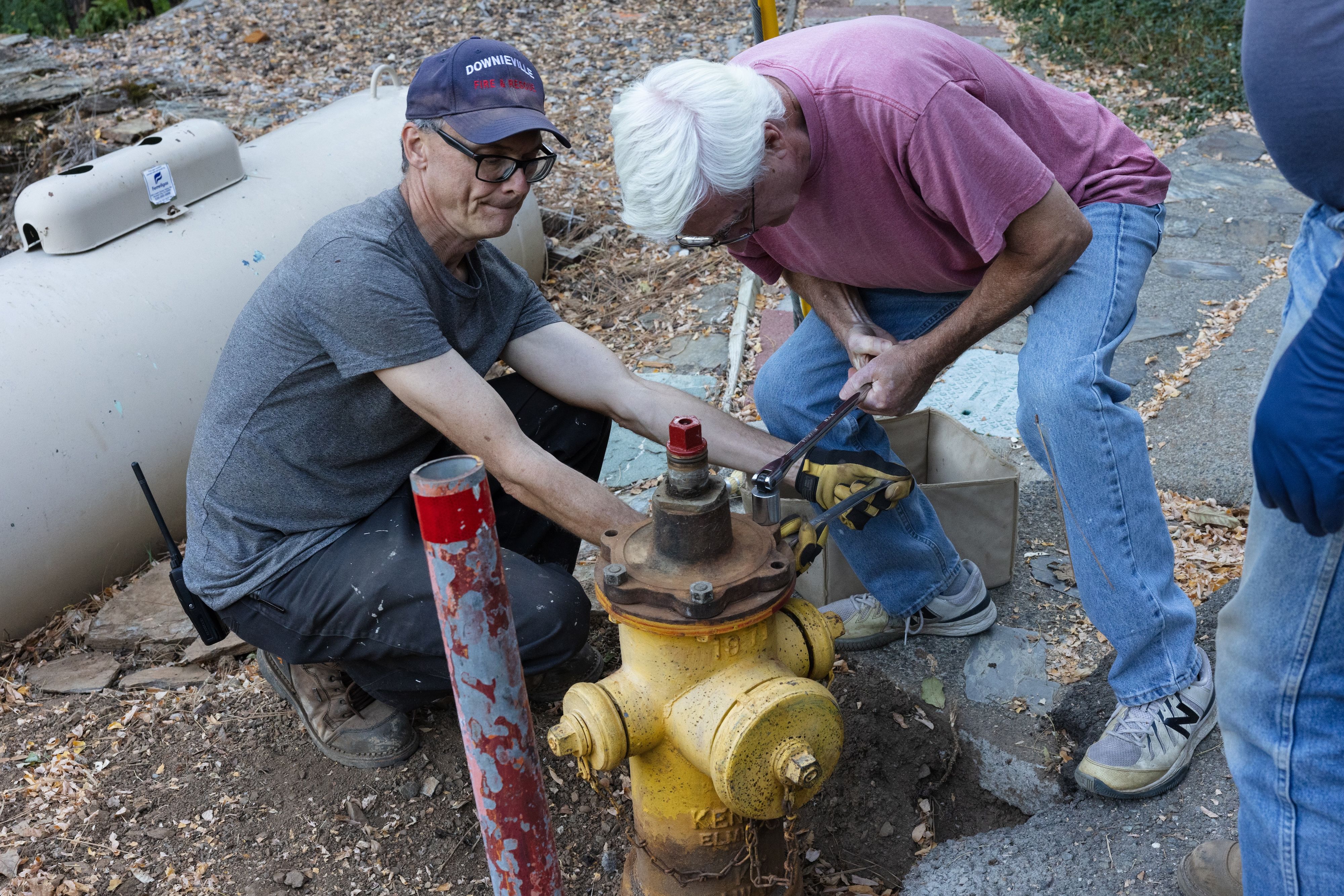 Keith Loving and Paul Douville unscrew a cap at the top of the hydrant
