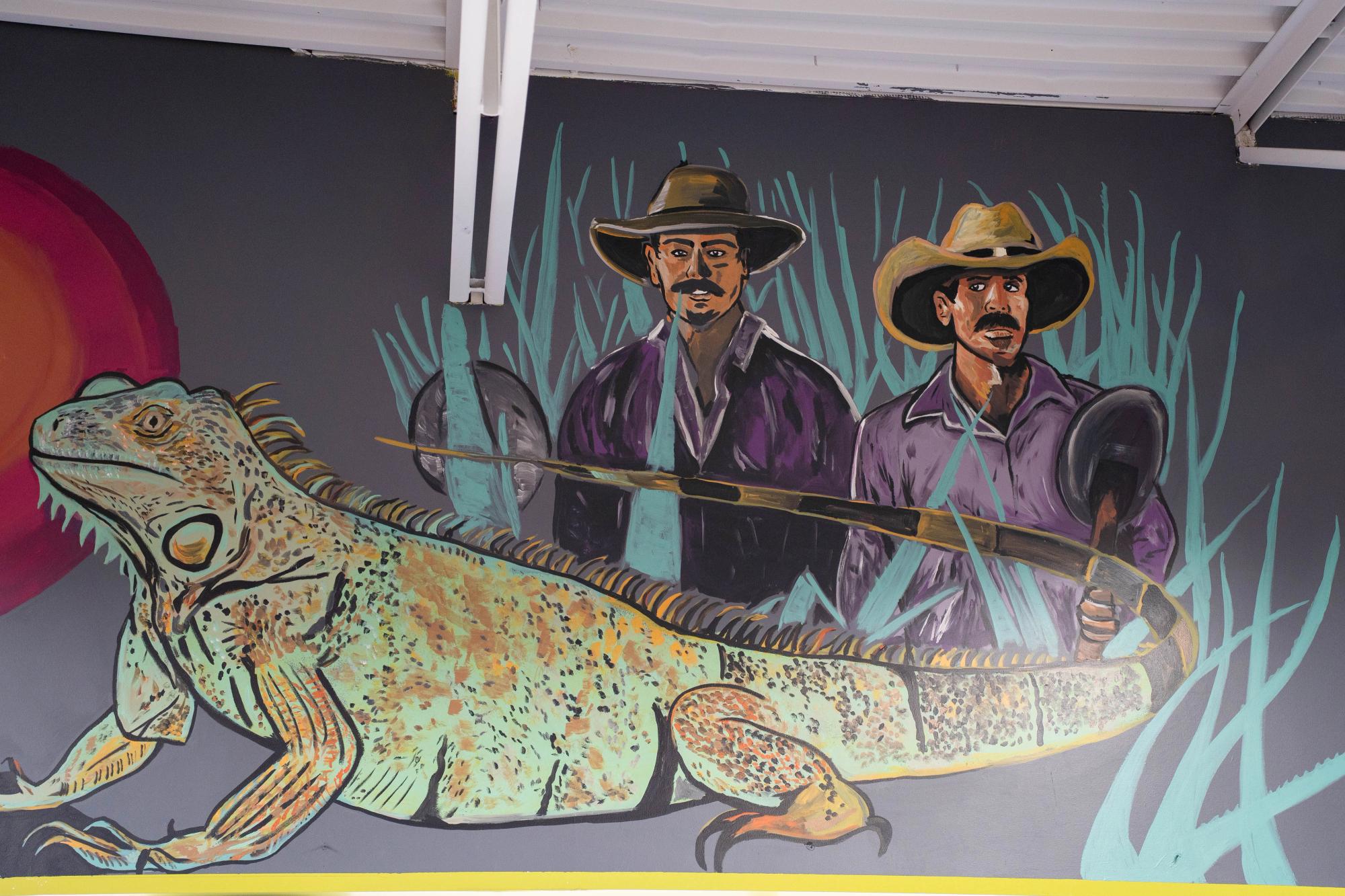 A lizard and two men (cowboys) stand behind a lizard on a bluish wall 