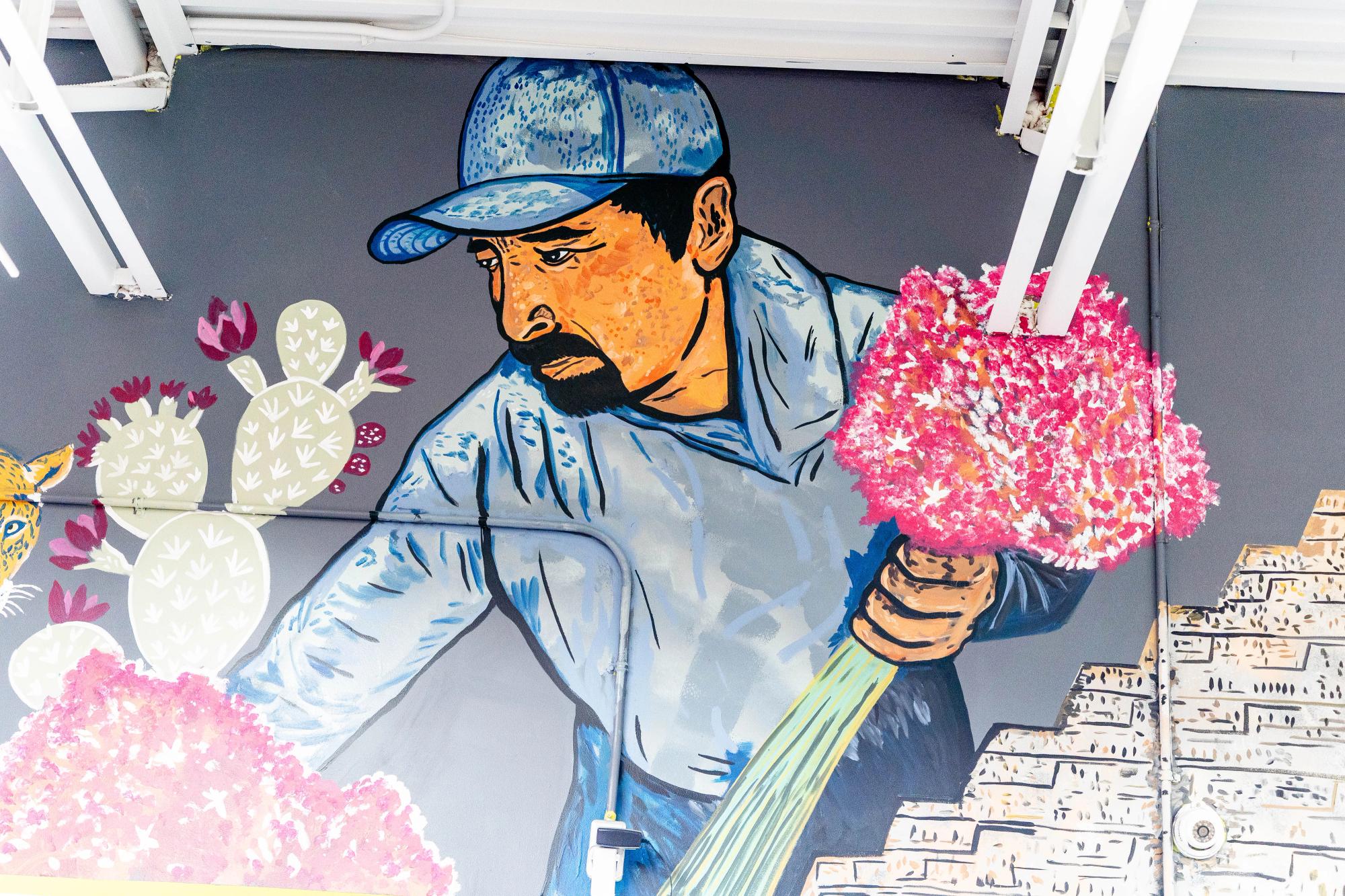 A man holding flowers in a blue shirt painted next to pyramids on a grey wall 