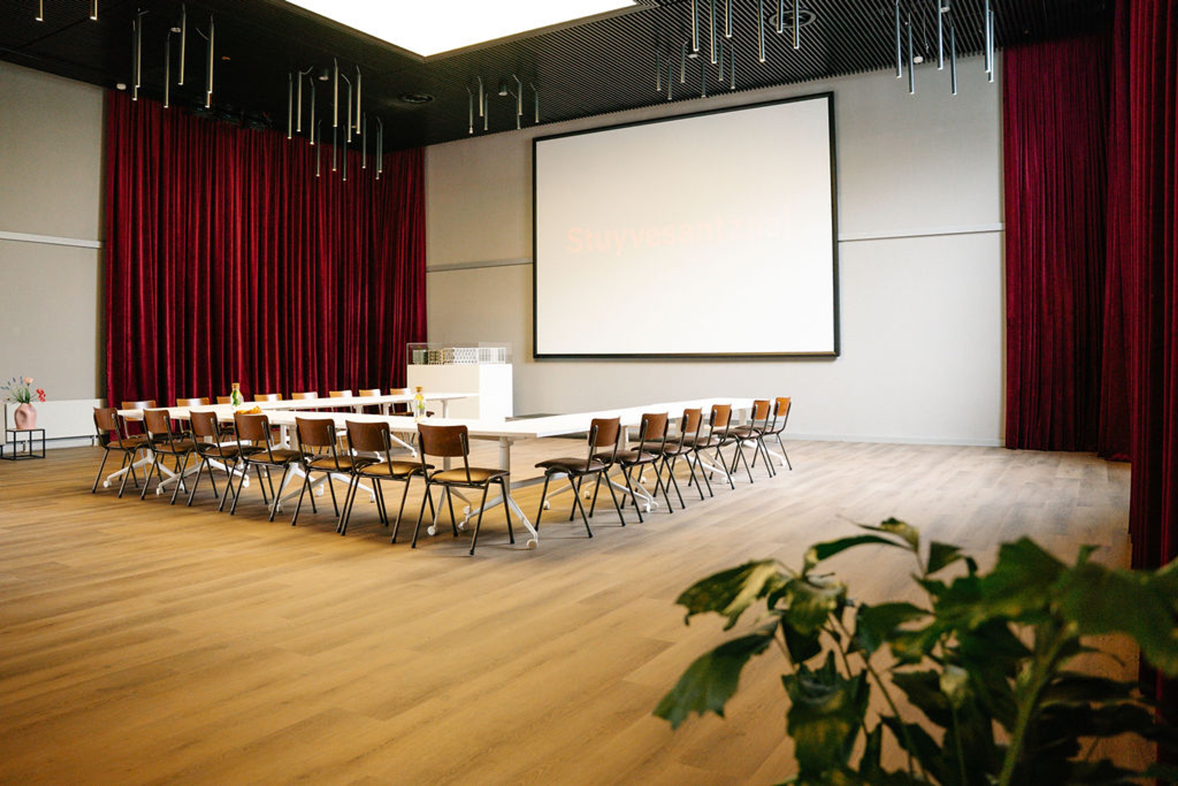 De Stuyvesantzaal met rode velours gordijnen en groot presentatiescherm