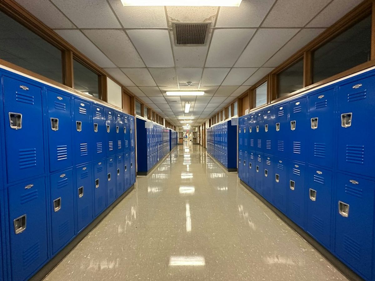 A long, empty school hallway lined with blue lockers.