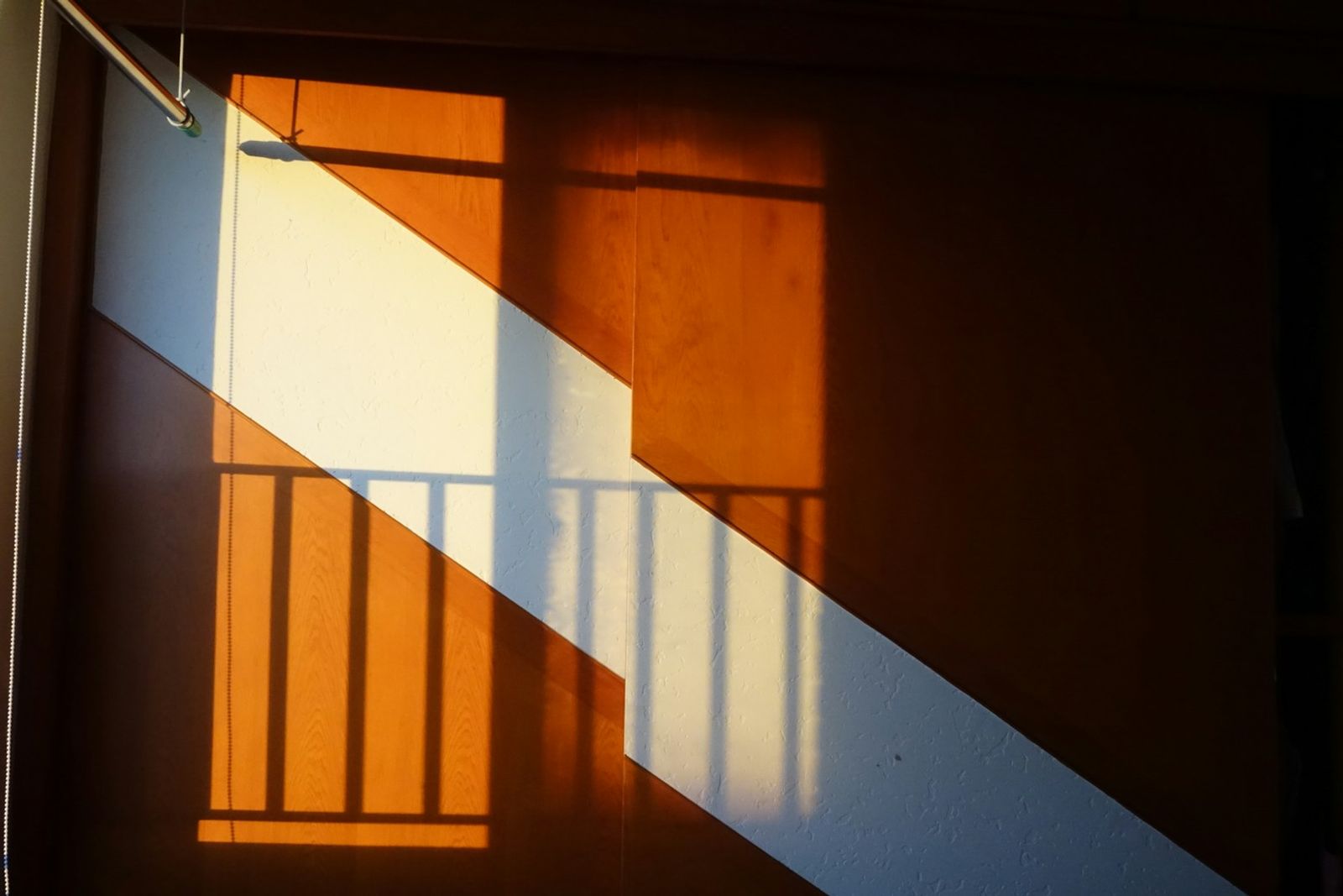 Diagonal sunlight and a railing shadow falling across a wooden wall