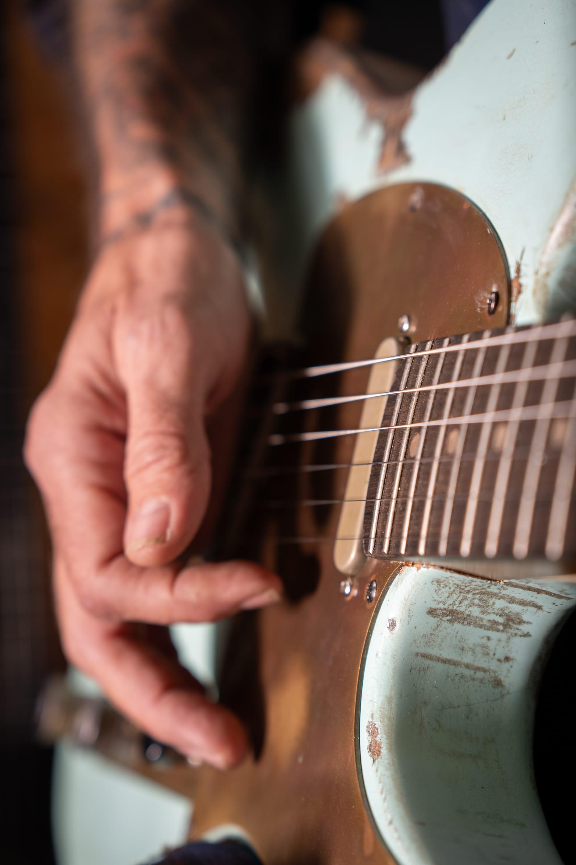 A hand on the strings of the Runaway, a pale green guitar with a brass pickguard, in the shed