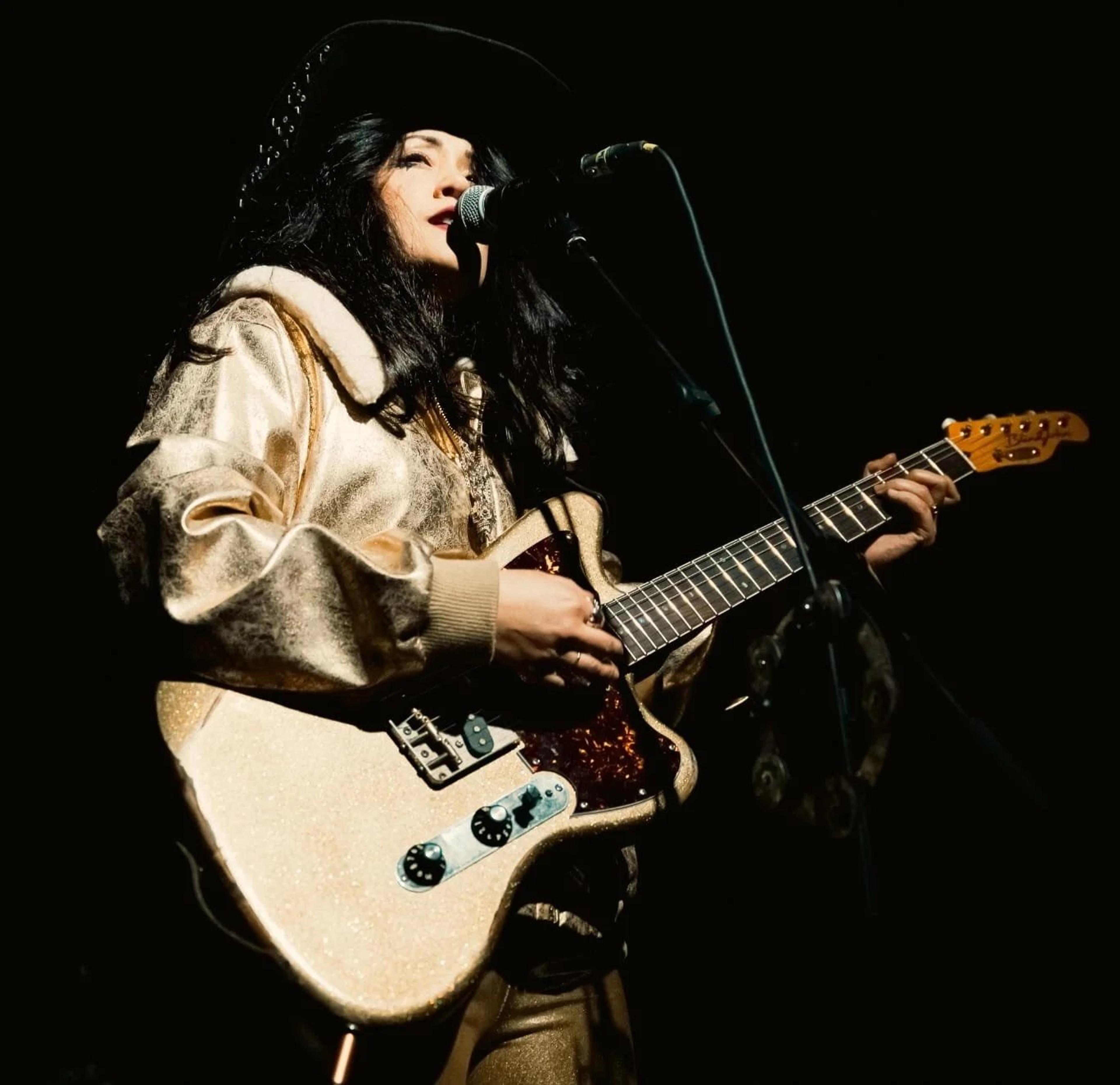 Zoe Devlin Love of Alabama 3 singing at the microphone, playing her Gen X — a gold flake offset with a tortoiseshell guard.