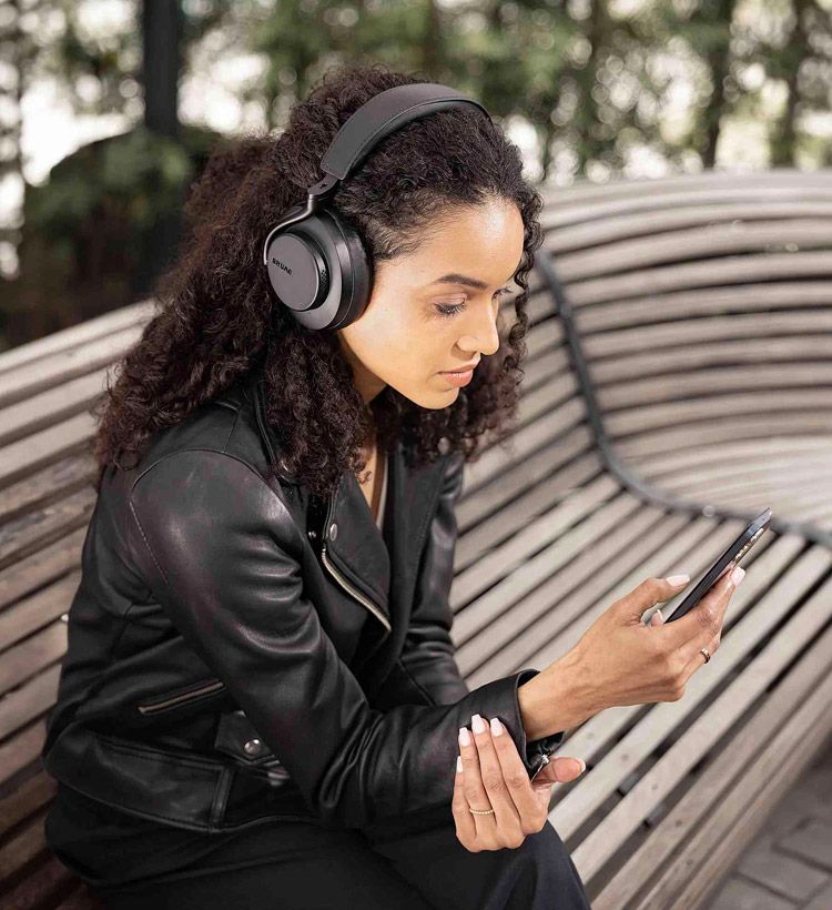 Woman sitting in a park wearing noise canceling headphones