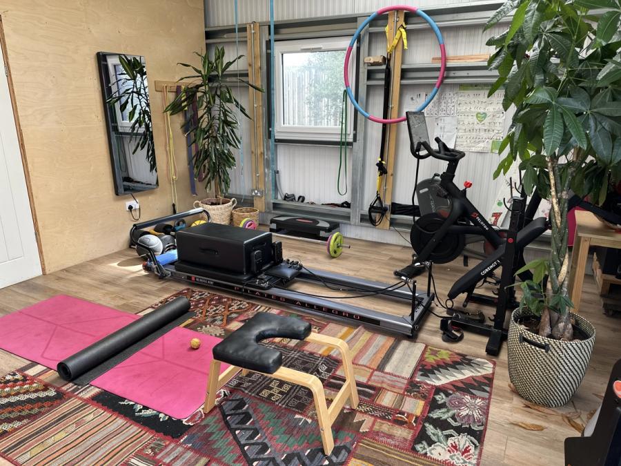 The gym in the shed at Bothan Jura Retreat, Isle of Jura, with a Pilates reformer, yoga inversion chair, Peloton bike and gymnastic rings