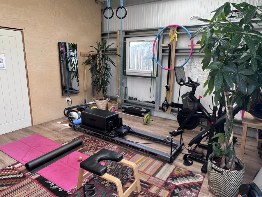 The gym in the shed at Bothan Jura Retreat, Isle of Jura — Pilates reformer, Peloton bike, gymnastic rings and free weights, seen across the whole room