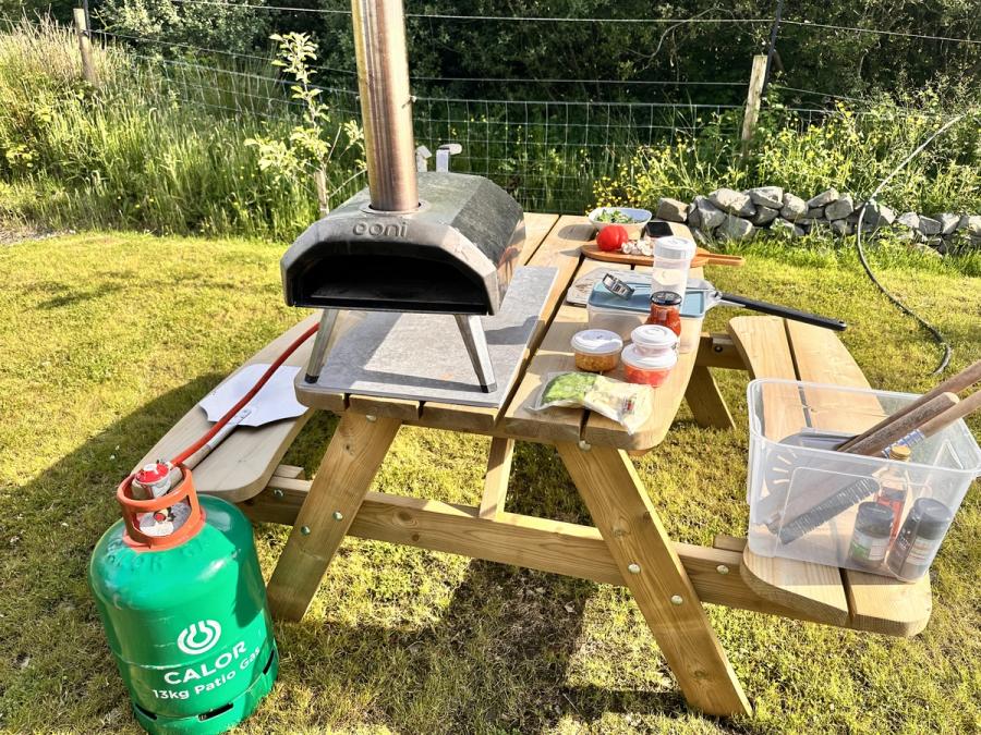 An Ooni gas-fired pizza oven on the picnic bench at Bothan Jura Retreat, Isle of Jura, with the gas bottle, peel and toppings laid out