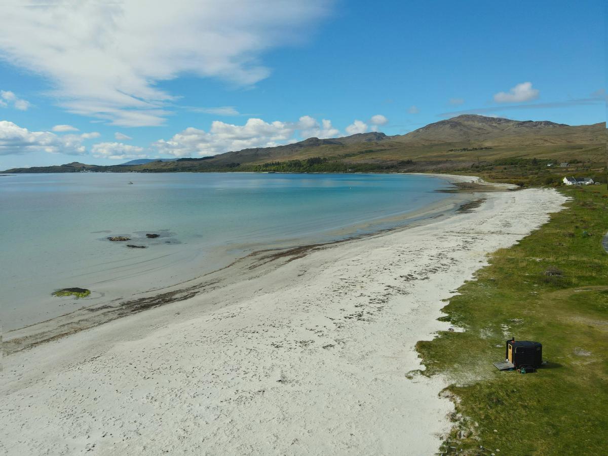 The wood-fired wild sauna parked above the white sand and turquoise water of Corran Sands, Isle of Jura