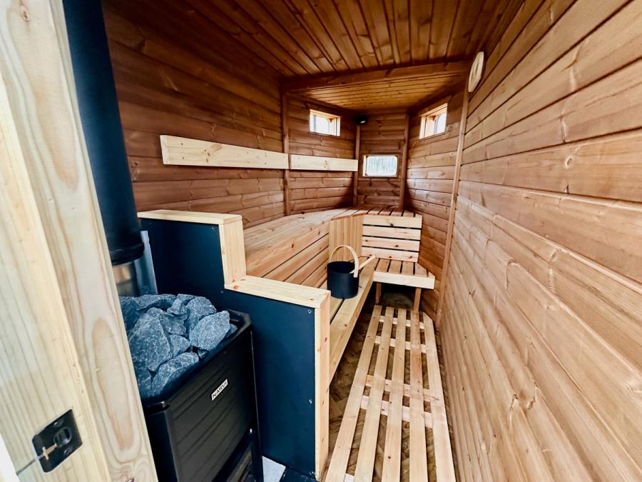 Inside the wild sauna: cedar benches, a Narvi wood-burning stove topped with rocks, and a water bucket