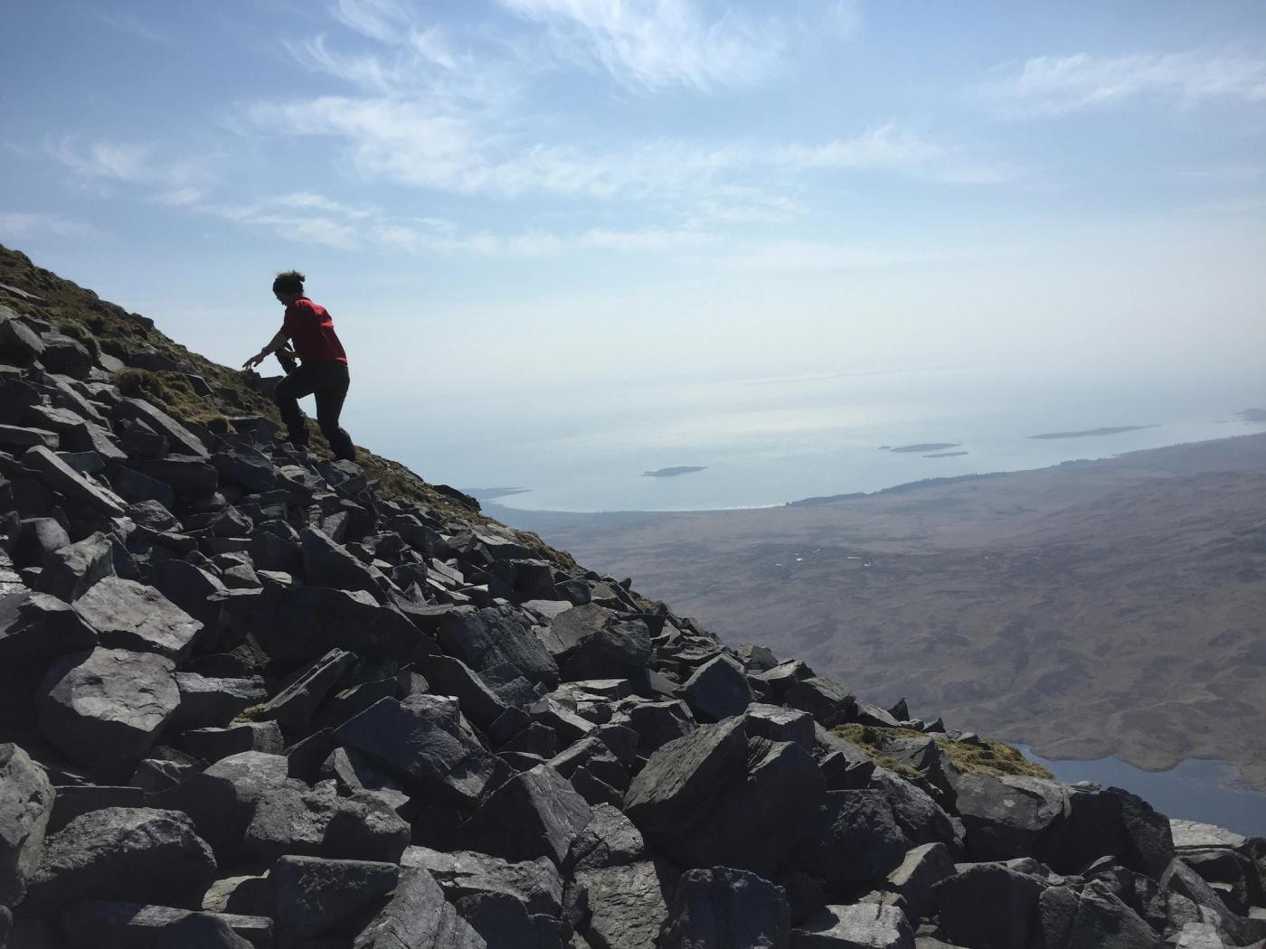 A walker climbing the boulder field high on the Paps of Jura, the moor and the sea far below