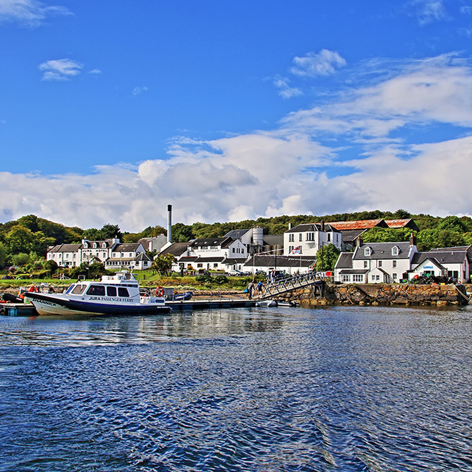 The Jura Passenger Ferry catamaran alongside the pier at Craighouse, Isle of Jura, with the Jura Hotel and Jura Distillery behind