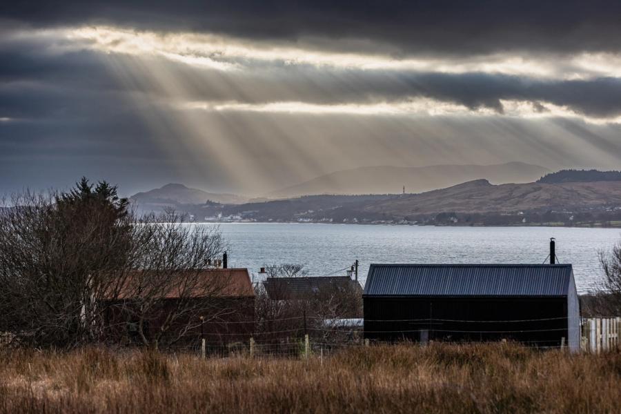 The Black Hut and The Rusty Hut at Bothan Jura Retreat, Knockrome, Isle of Jura, with the Sound of Jura and the mainland hills behind under breaking light