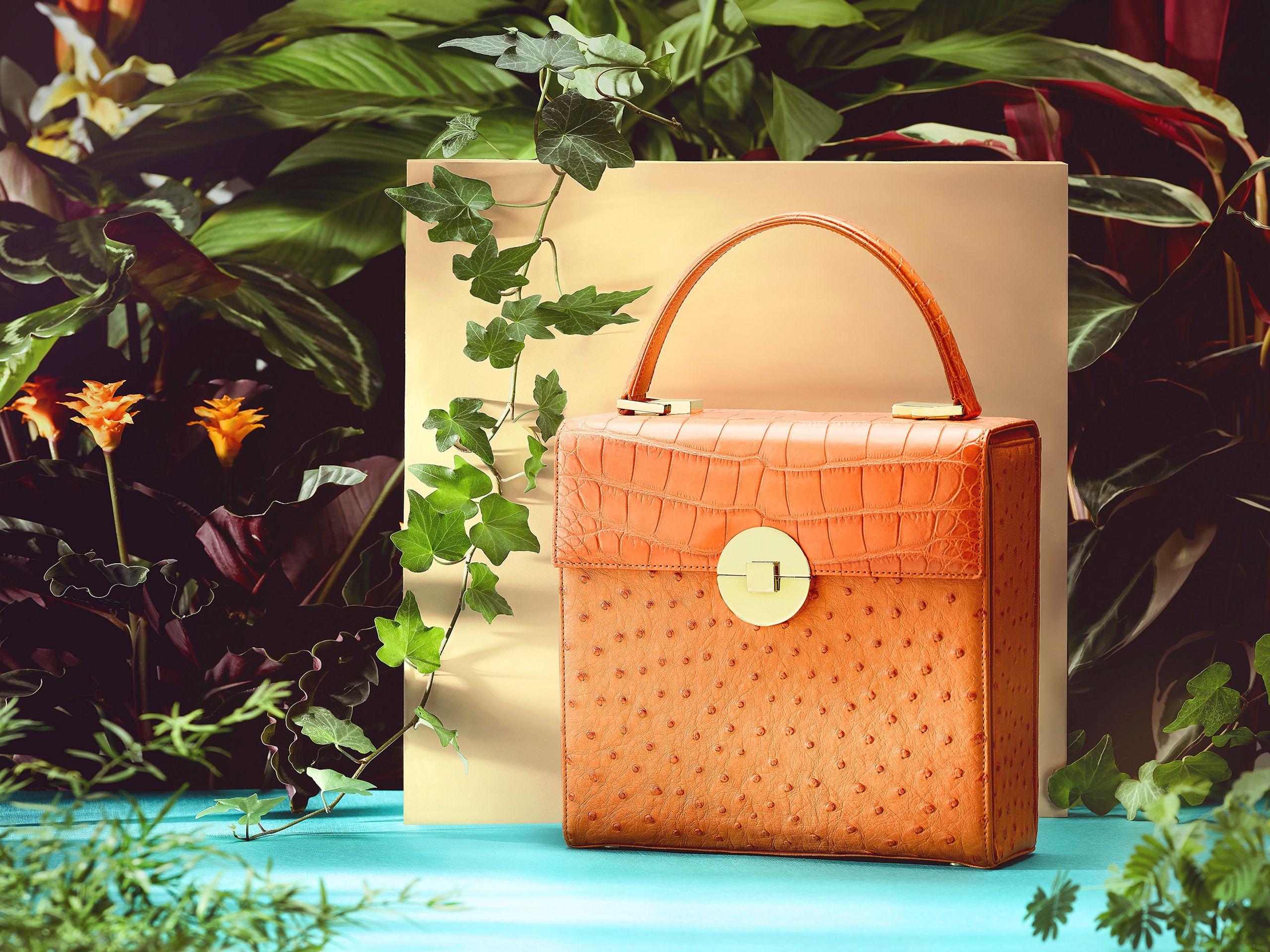 Orangefarbene Handtasche in einem botanischen Stillleben