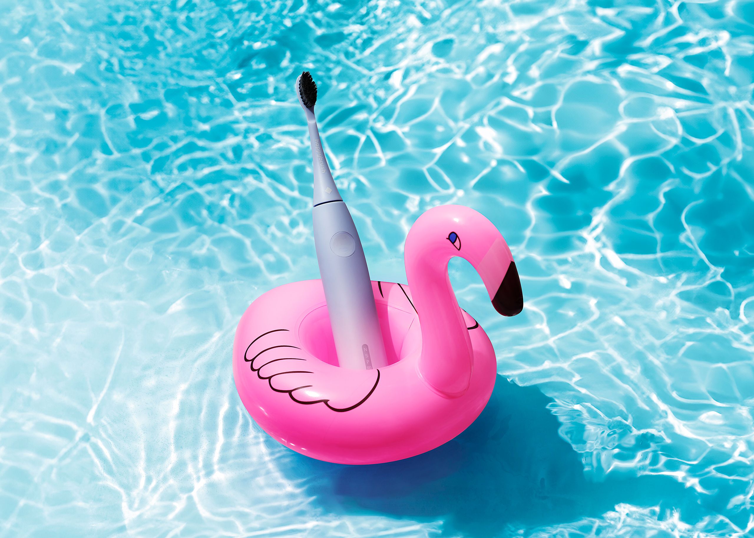 happybrush Zahnbürste auf rosa Flamingo-Schwimmring im türkisblauen Pool