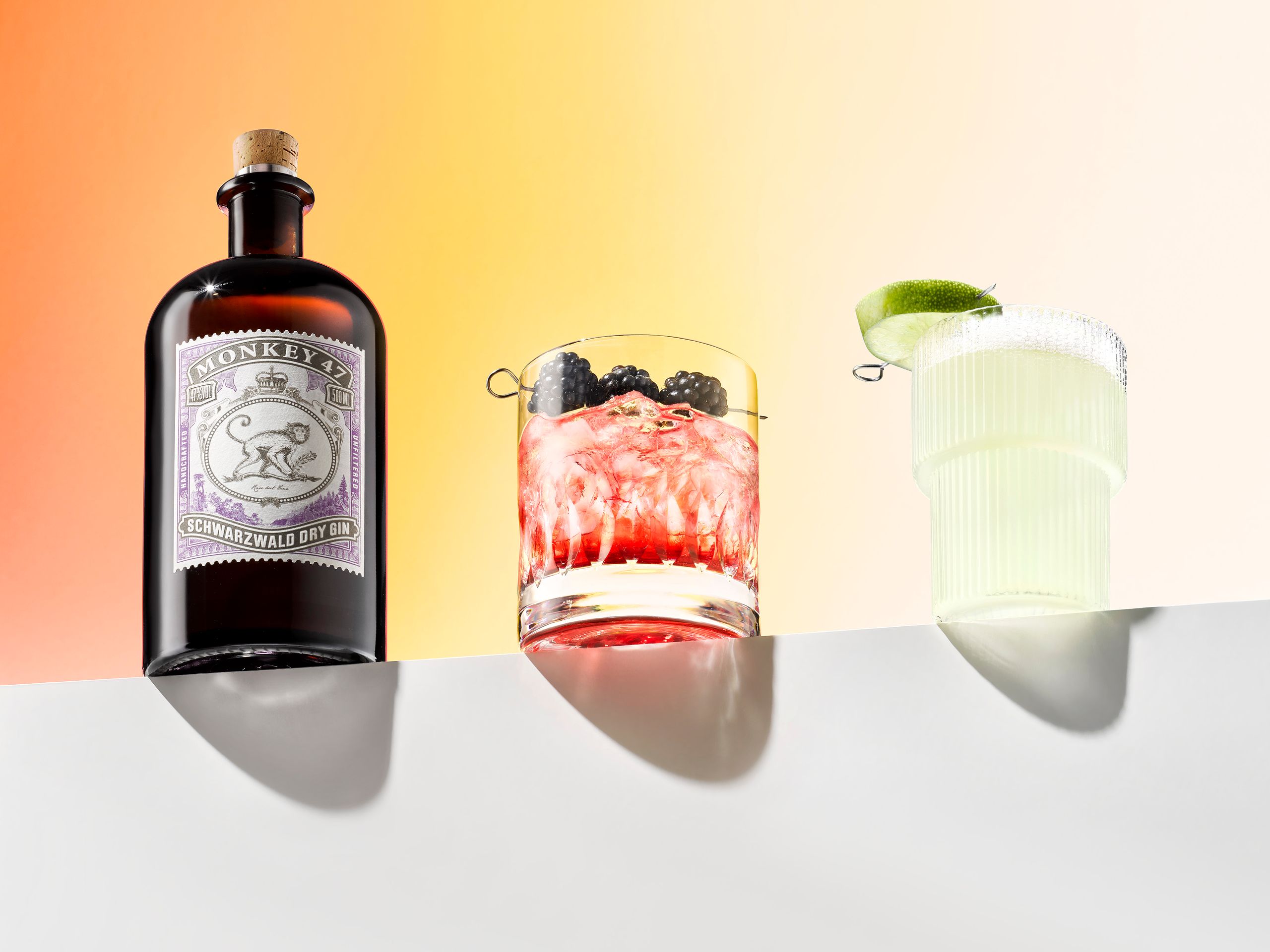 Monkey 47 Gin mit zwei Drinks vor warmem Farbverlauf