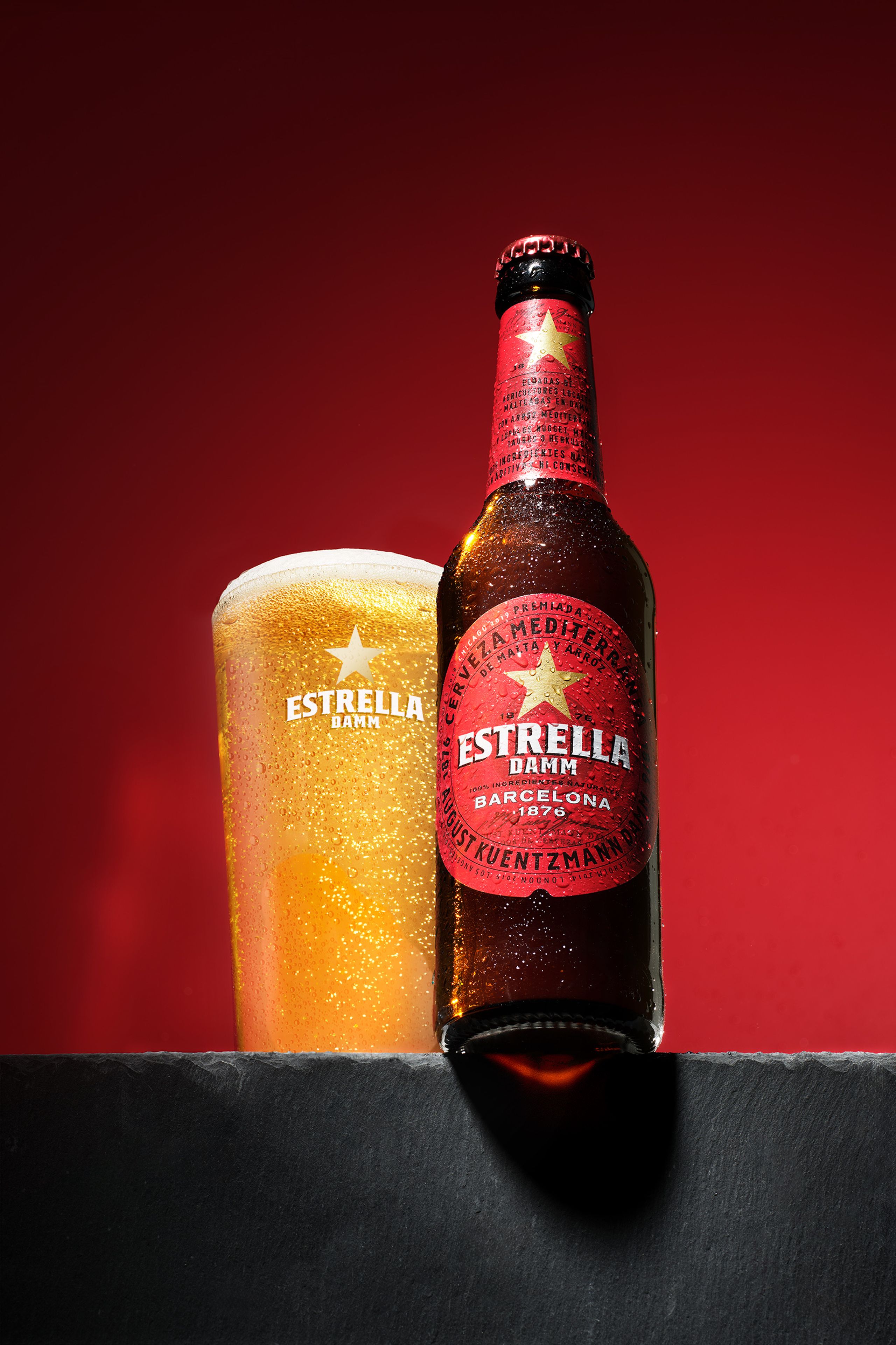 Estrella-Bierflasche und gefülltes Glas vor rotem Hintergrund