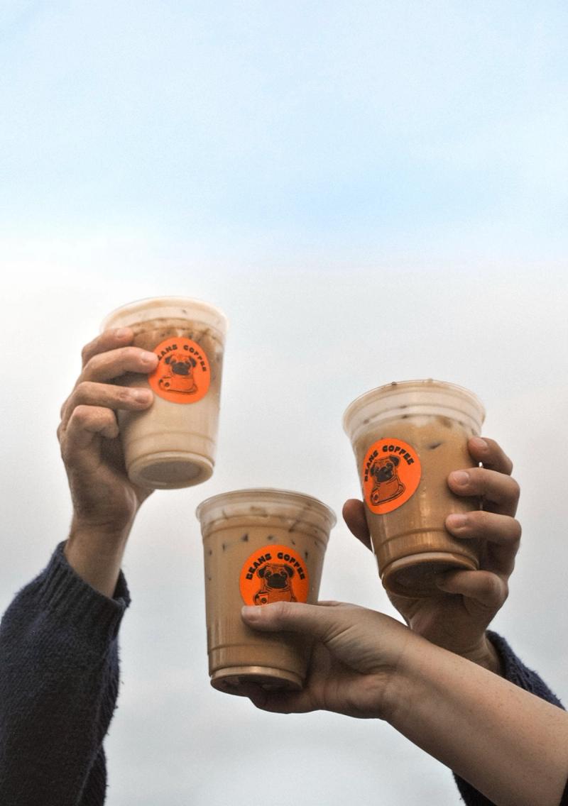 Three Beans coffee latte with Beans coffee pug sticker against the sky