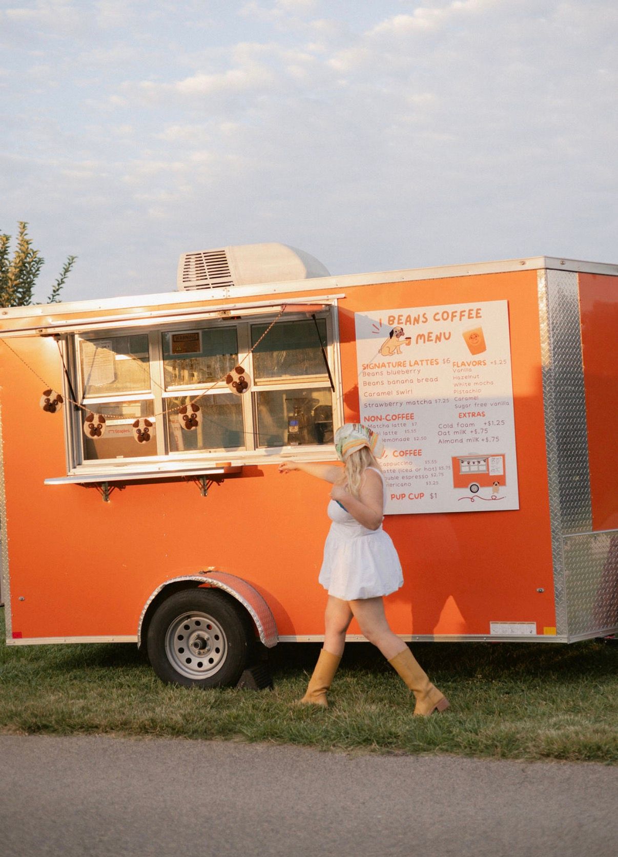 An orange trailer with a Beans Coffee menu and a woman standing in front of it
