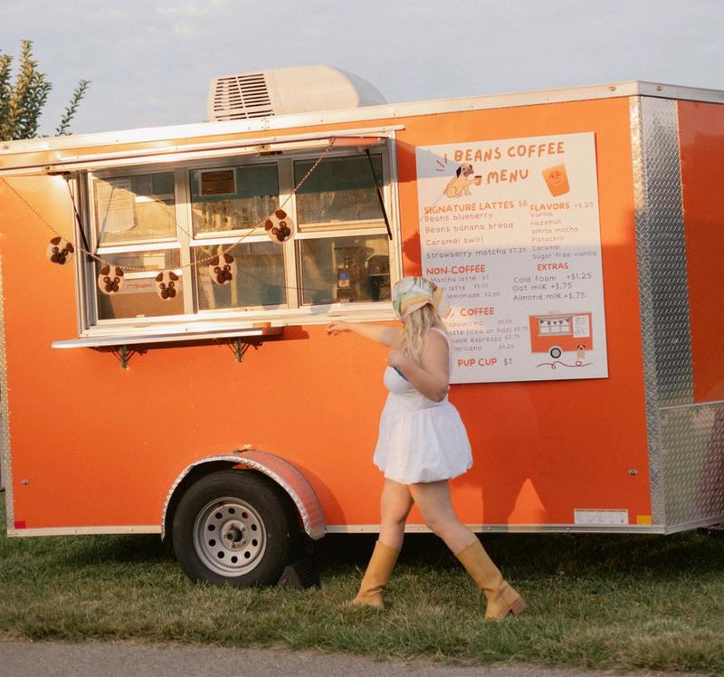 An orange trailer with a Beans Coffee menu and a woman standing in front of it