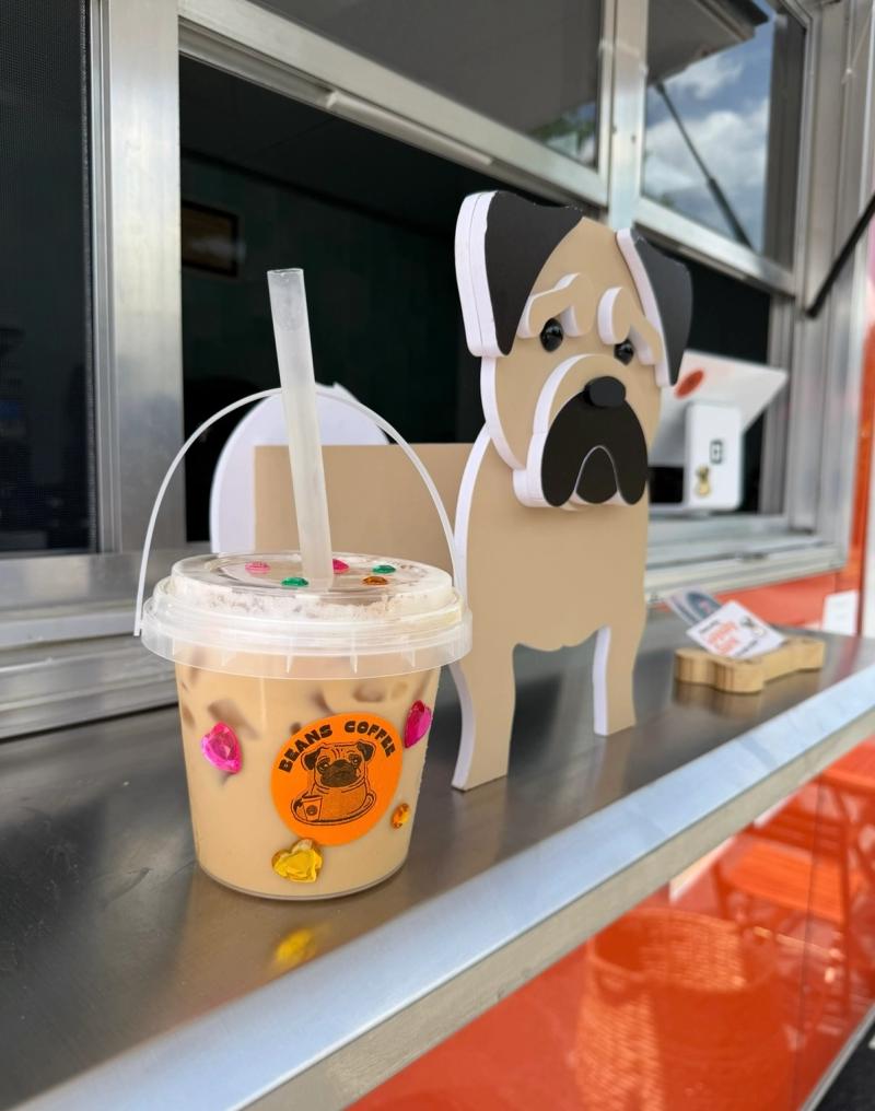 A Beans Coffee bucket drink next to a pug foam cutout on the windowsill of the trailer