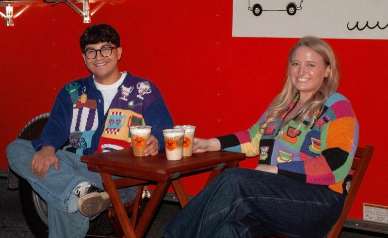 Cassidy and Brian sitting either side of a folding table at the cart, three cups between them