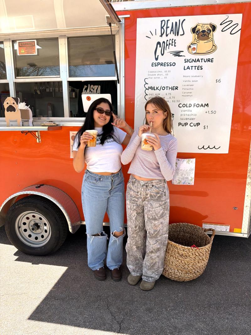 Two women standing in front of the Beans Coffee trailer drinking coffee