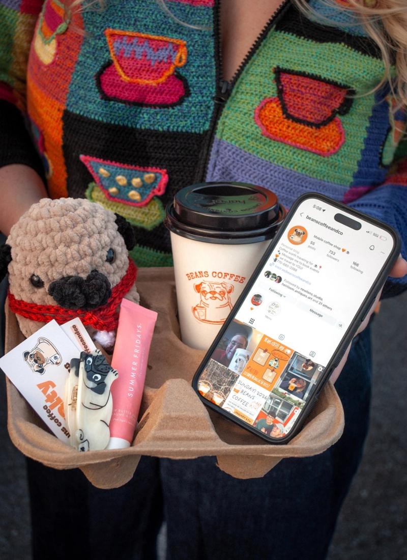 Coffee takeout tray of crochet pug, latte, cards, and an iPhone with Instagram opened