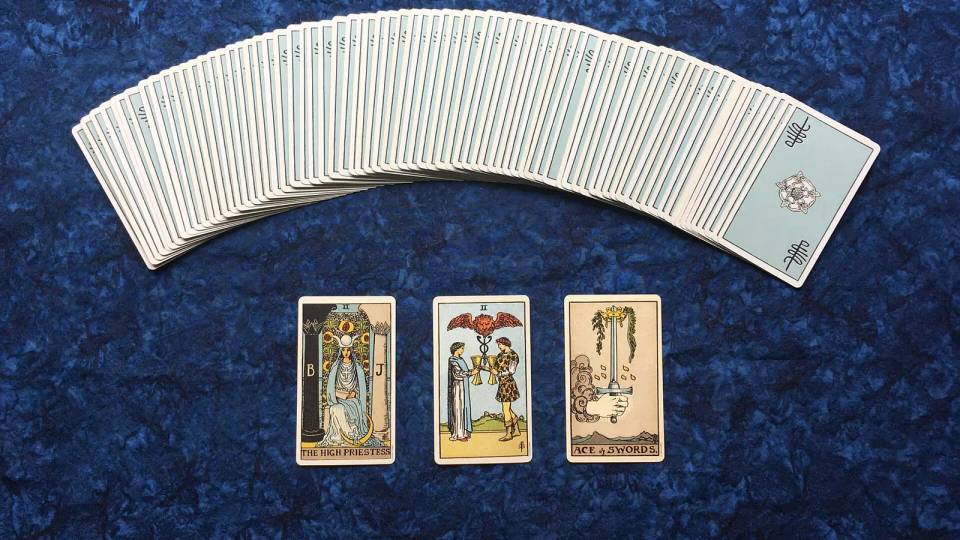 Lacivert örtü üzerinde yelpaze gibi açılmış tarot destesi ve önüne açılmış üç kart, tarot evet hayır falı için