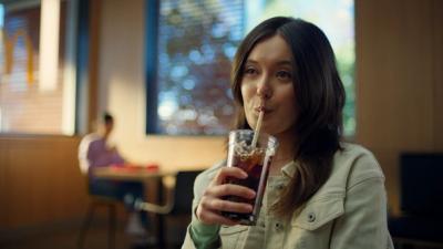 A young woman drinks from a cup of soda. 