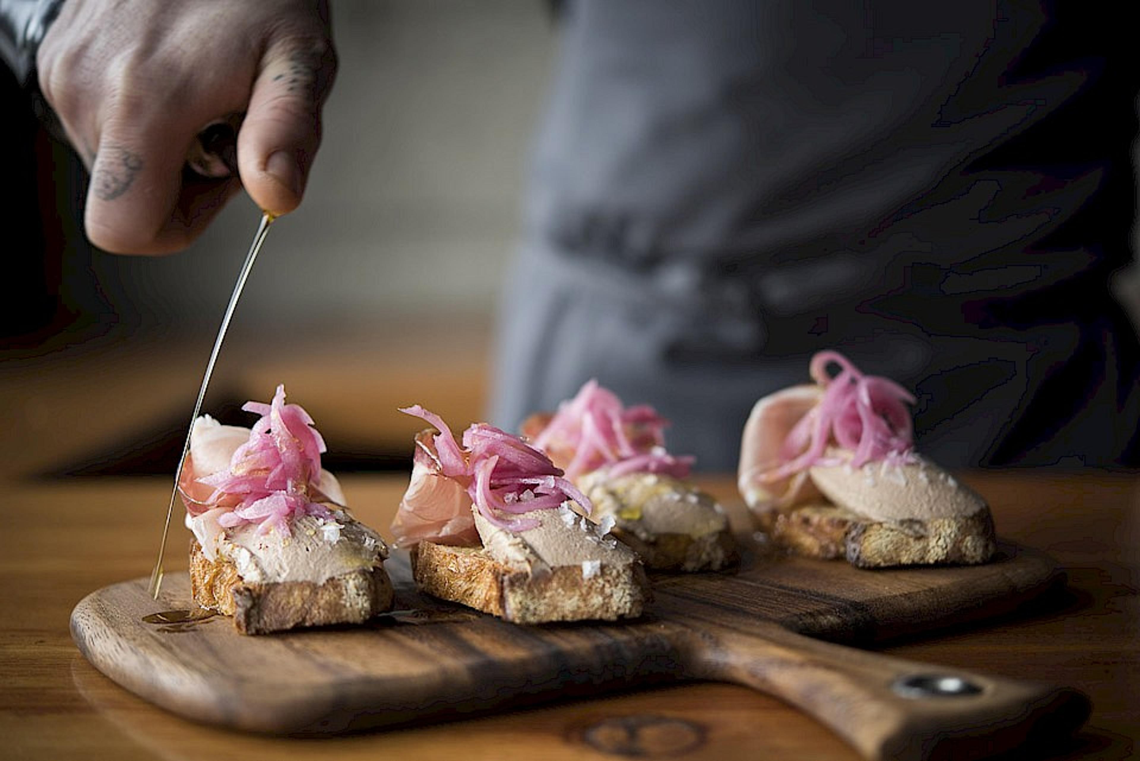 Chef topping chicken liver mousse, pickled onion bruschetta