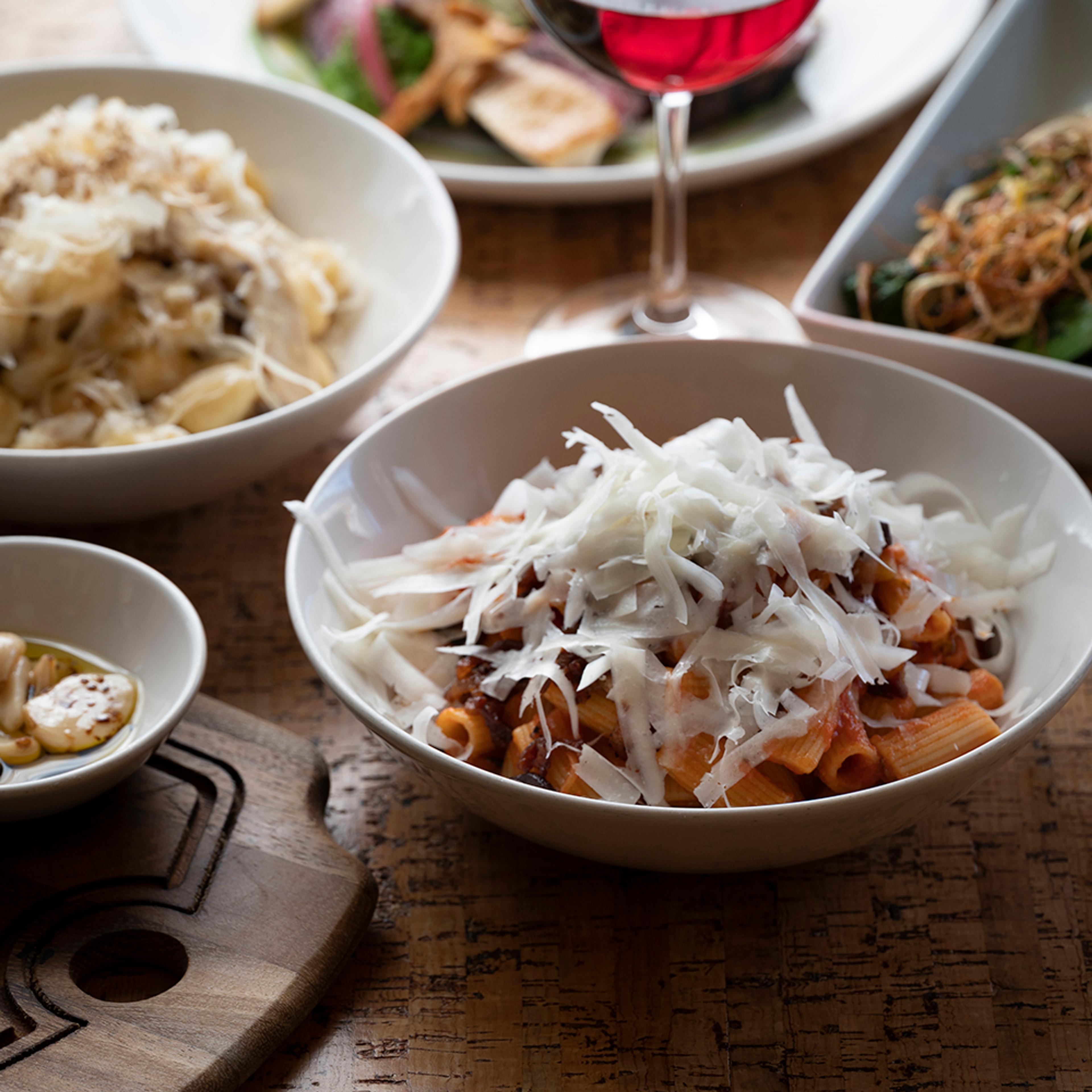 rigatoni bolognese surrounded by wine and pasta