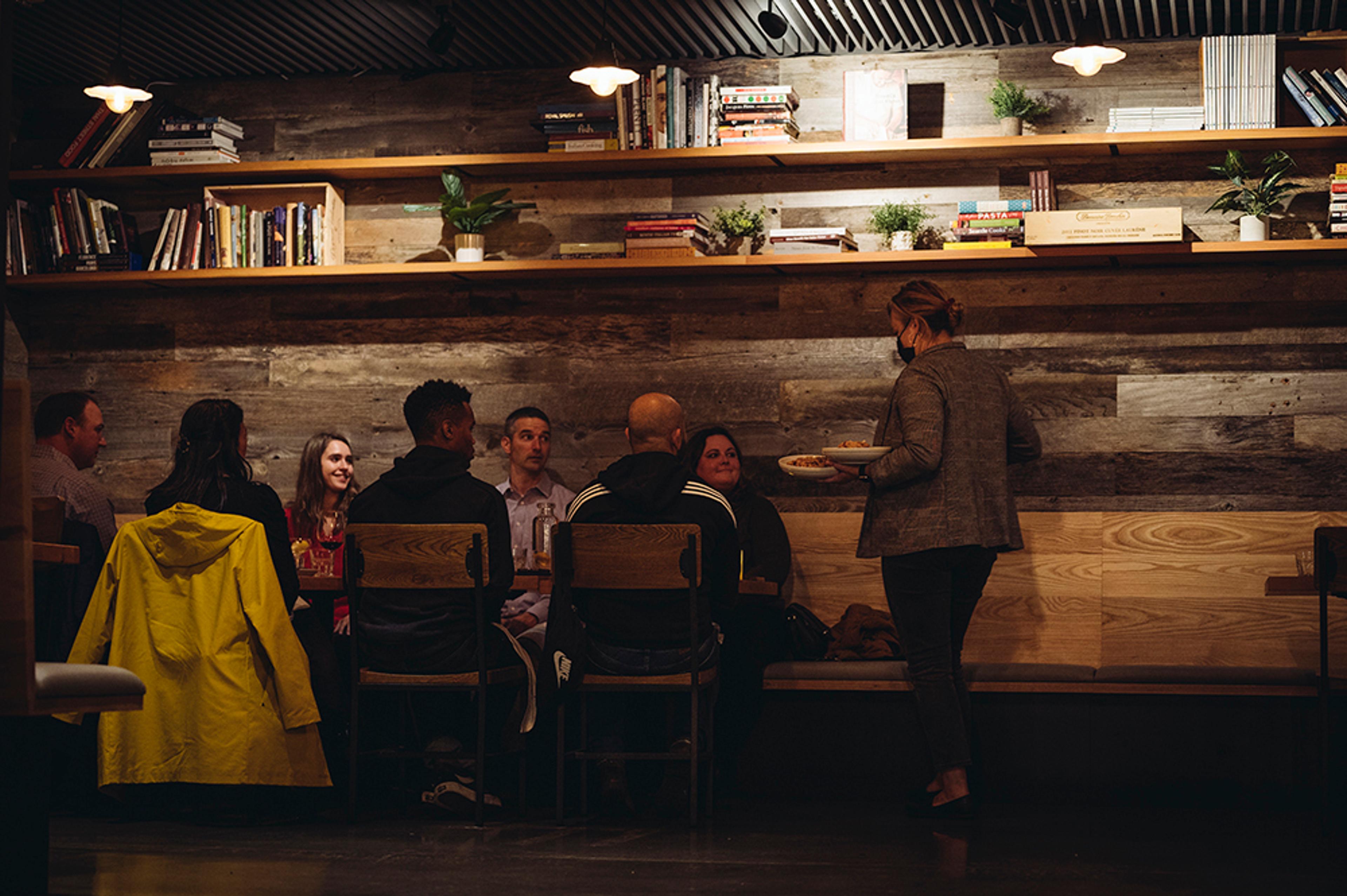 Manager serving food to large party in front of reclaimed wood wall