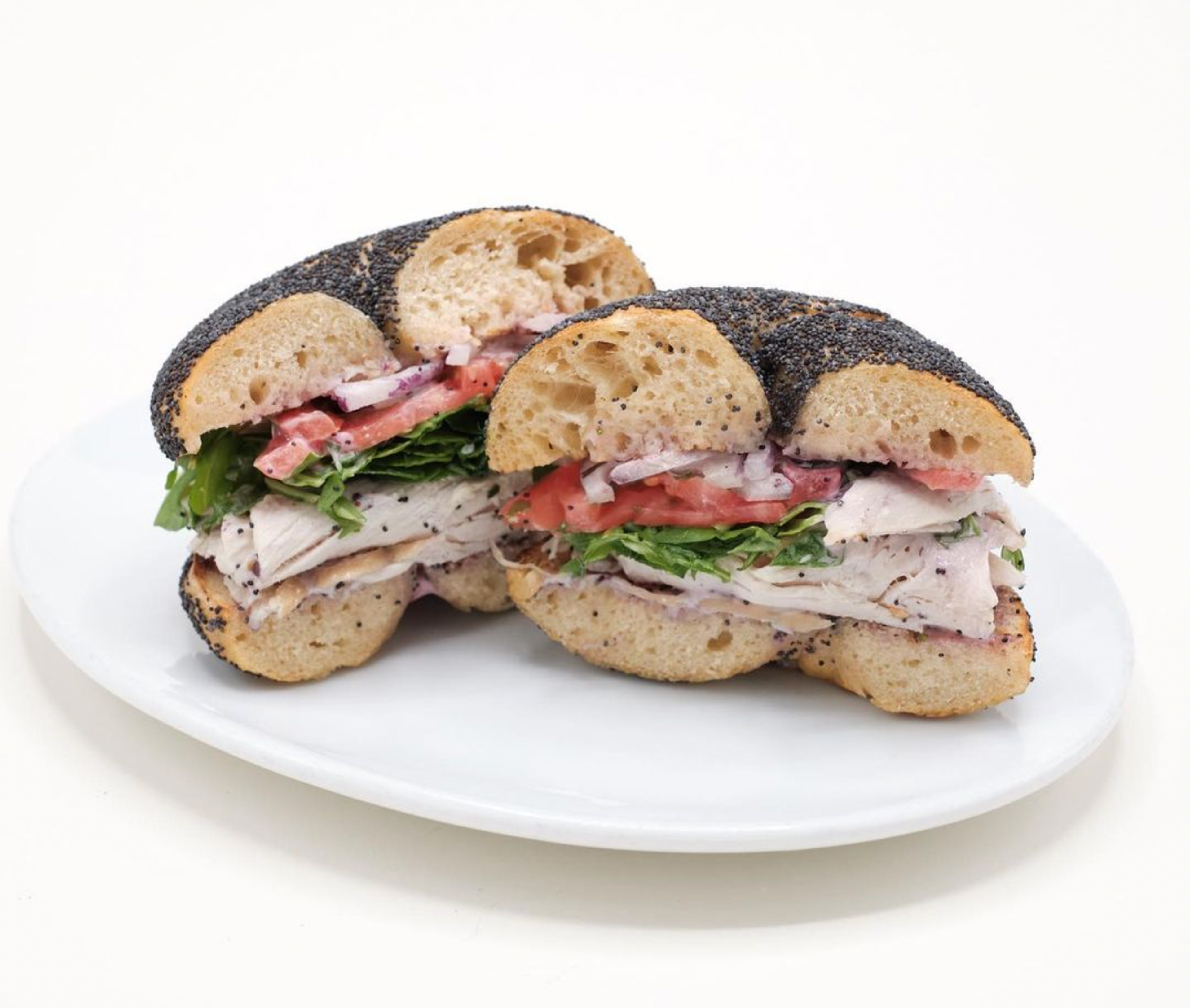 turkey bagel sandwich on a poppy seed bagel with tomato, onion, arugula, and turkey