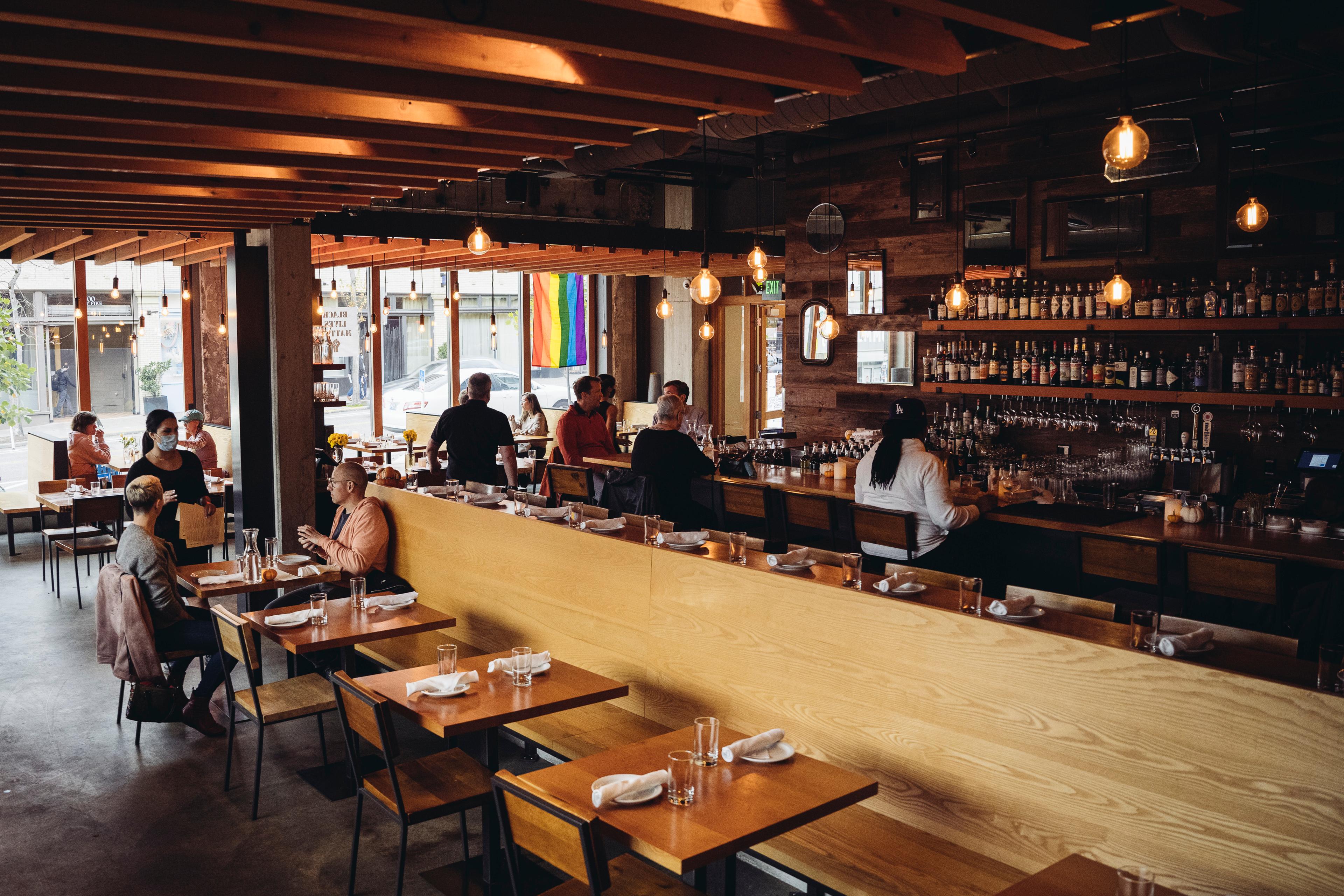 A large room with wood accents and a row of tables in front of a chic bar.